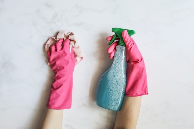 Cropped image of someone wearing pink gloves holding a blue spray bottle and towel